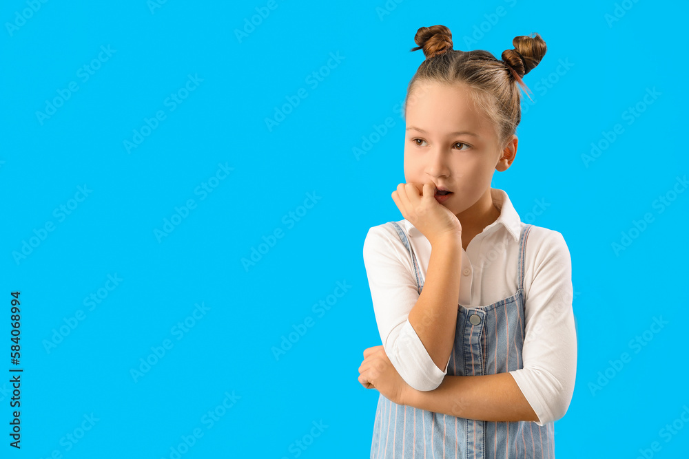 Little girl biting nails on blue background