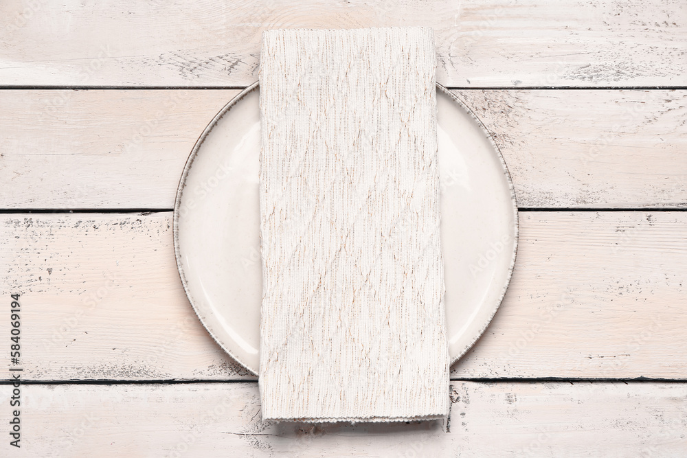 Plate with folded napkin on light wooden background