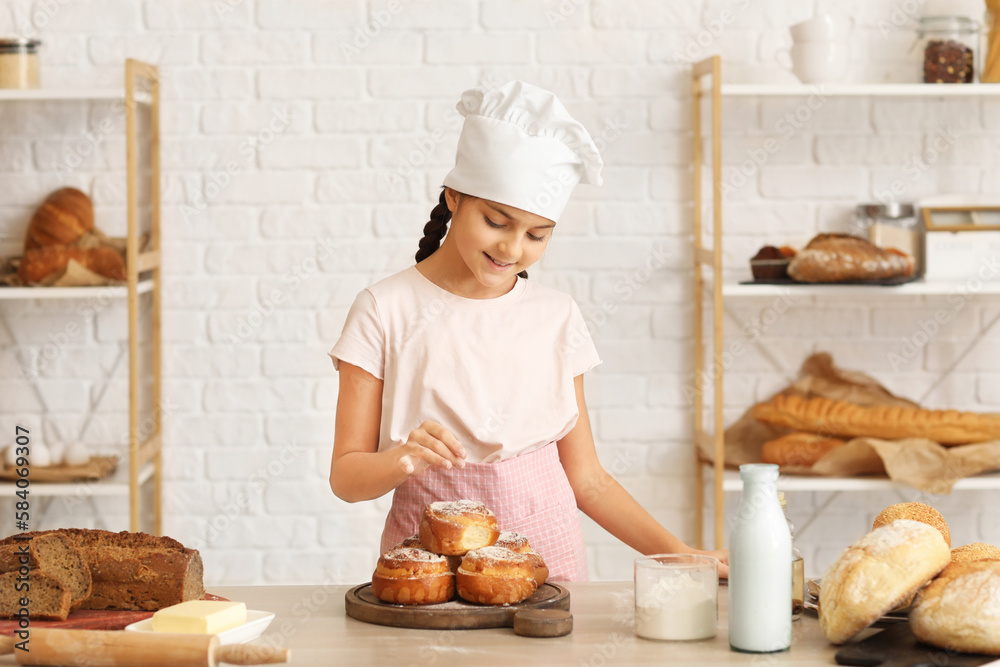 Little baker sprinkling sugar powder onto buns in kitchen