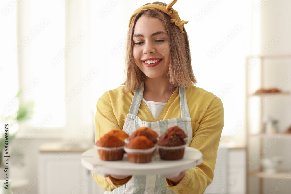 Female baker with tray of tasty cupcakes in kitchen