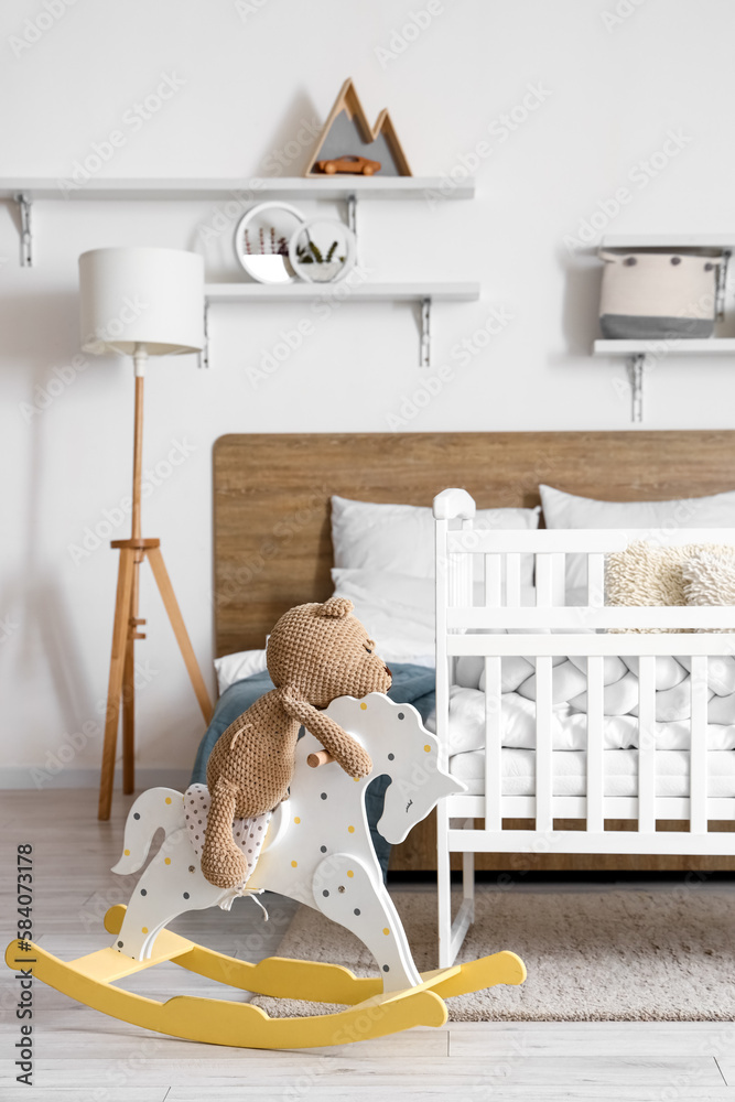 Interior of light bedroom with bed, baby crib and toys