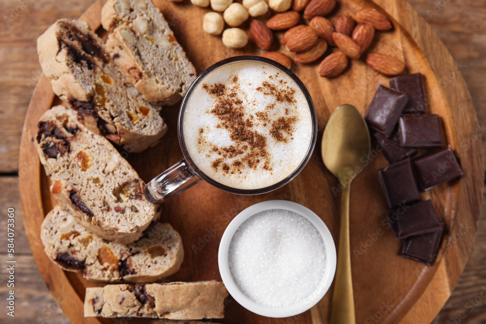 Board with delicious biscotti cookies, nuts, chocolate and cup of coffee on wooden background