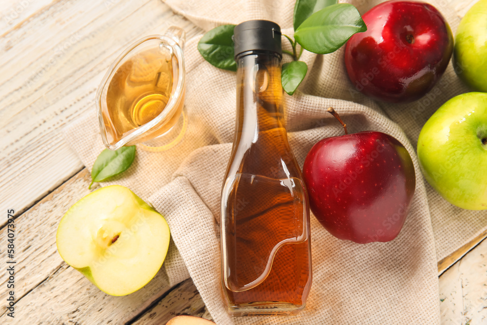 Glass bottle and gravy boat with fresh apple cider vinegar on white wooden background