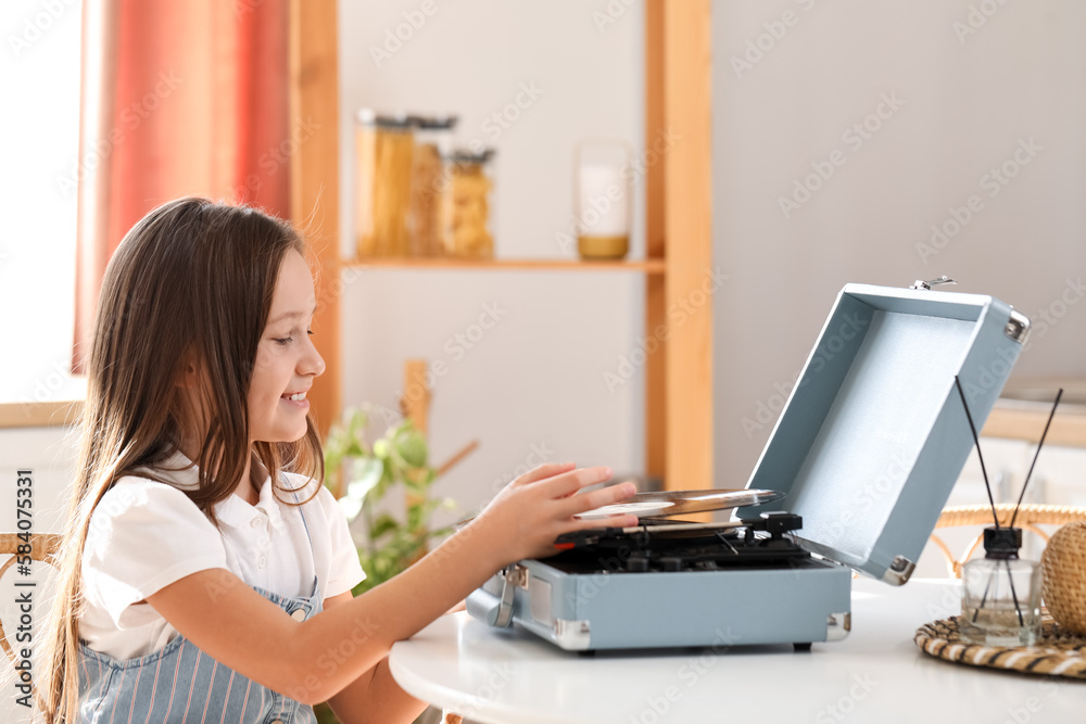 Little girl with vinyl disc and record player at table in kitchen