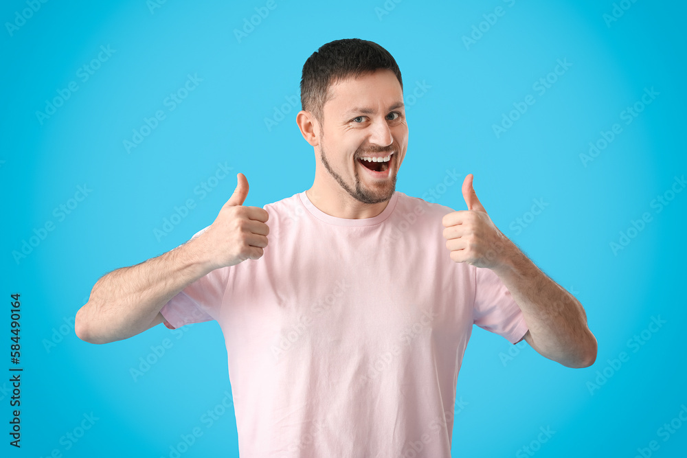 Handsome man in t-shirt showing thumbs-up on blue background