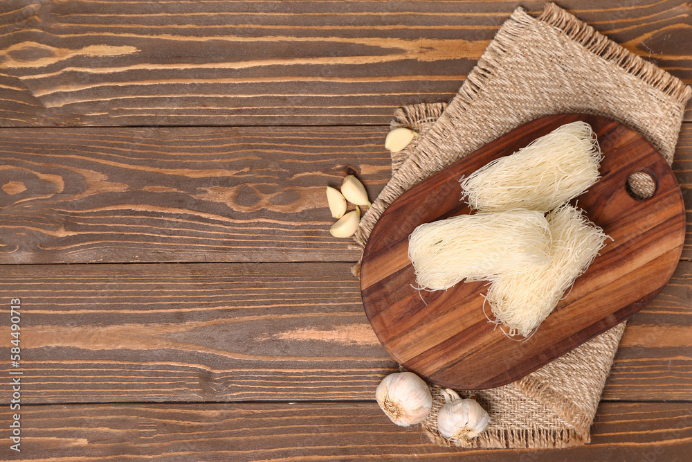 Board with raw rice noodles and garlic on wooden background