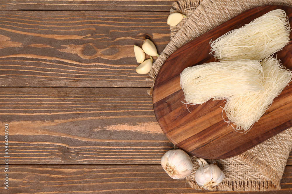 Board with raw rice noodles and garlic on wooden background