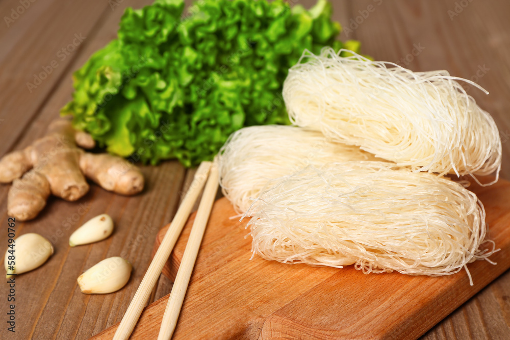 Board with raw rice noodles and chopsticks on wooden background