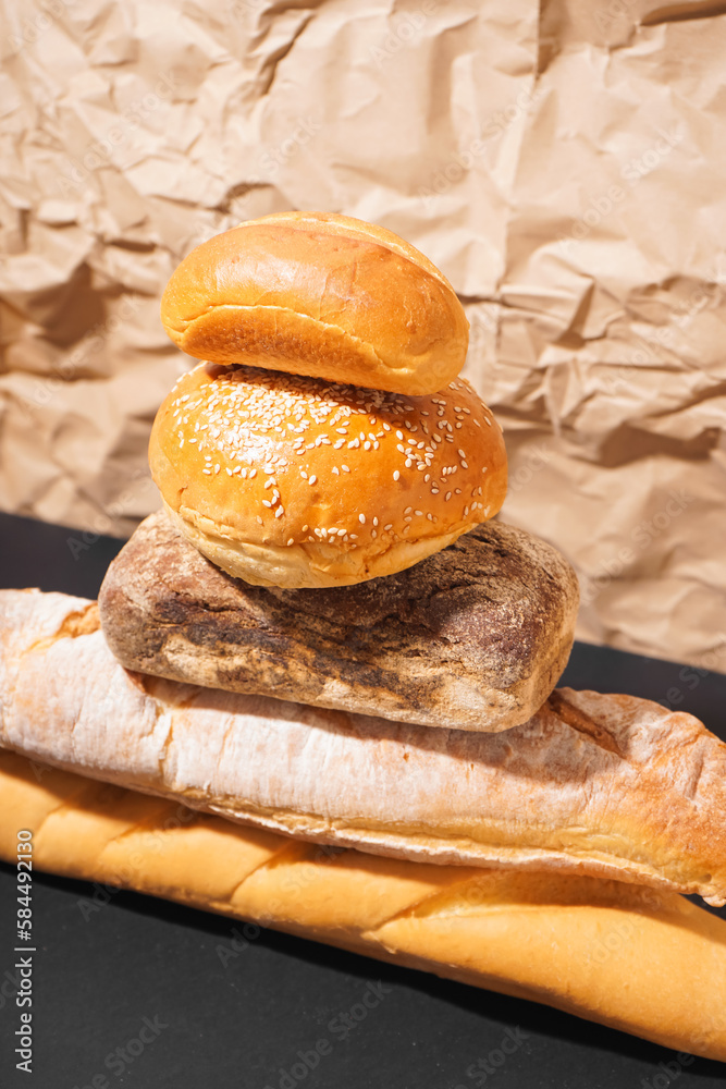 Stack of different fresh bread on black table near parchment