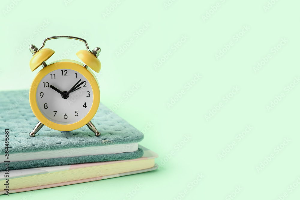 Notebooks and alarm clock on color background