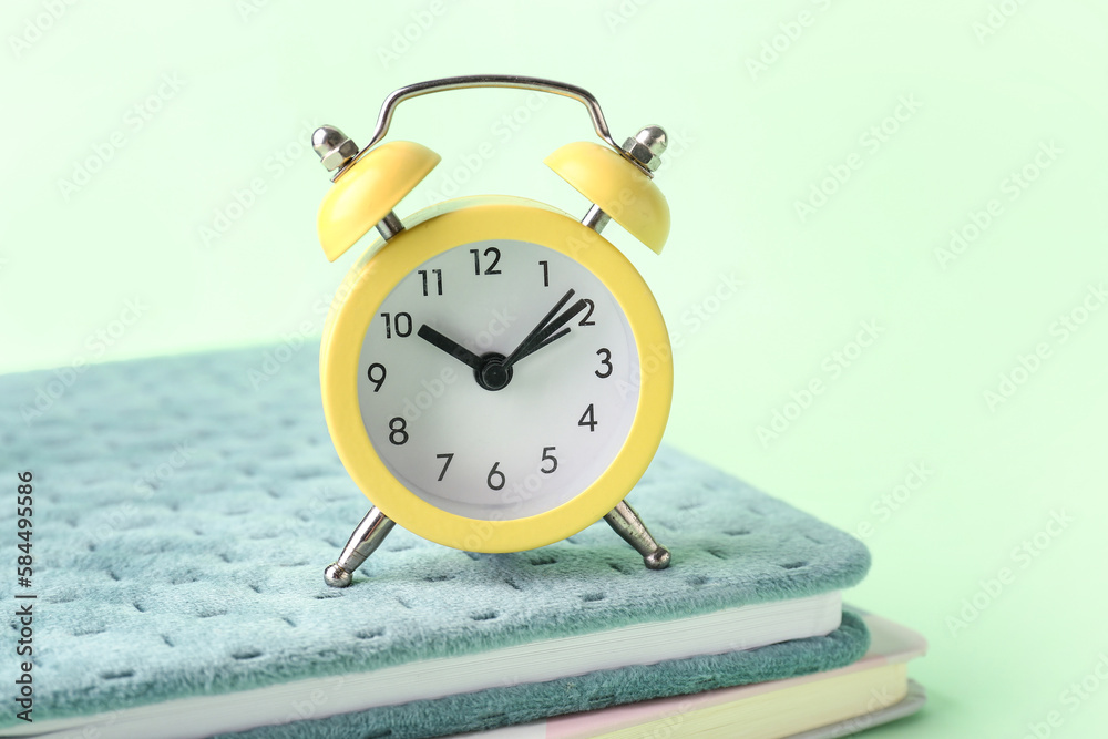 Notebooks and alarm clock on color background, closeup