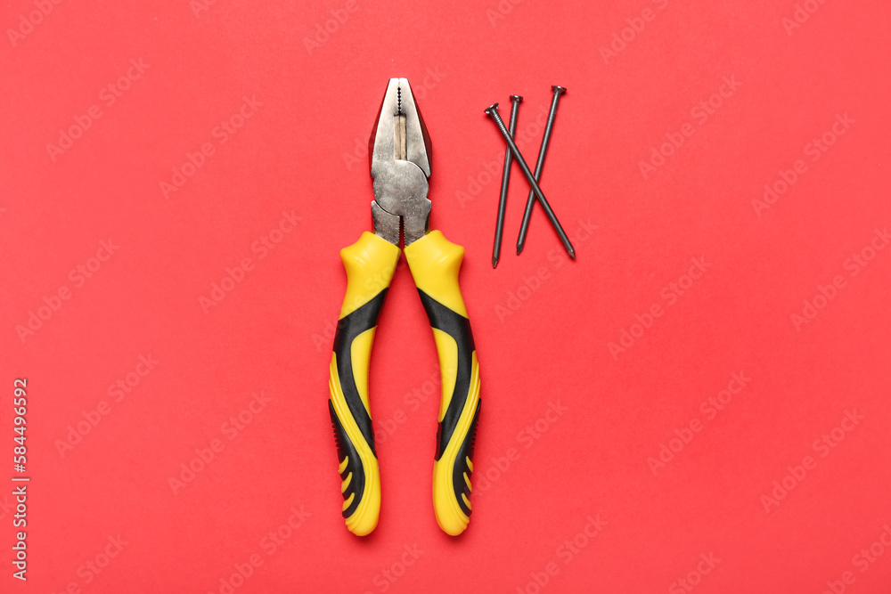 Pliers and nails on red background