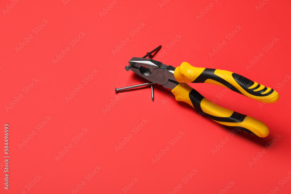 Pliers and nails on red background