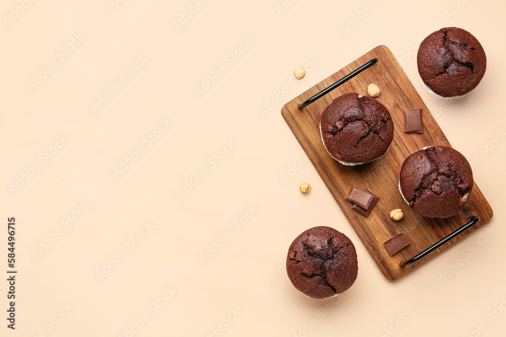 Wooden board with tasty chocolate cupcakes on beige background