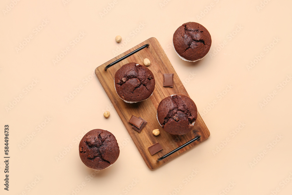 Wooden board with tasty chocolate cupcakes on beige background