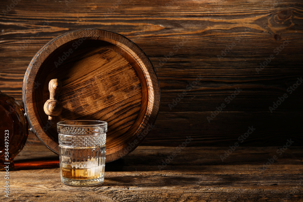 Glass of cold whiskey with oak barrel on wooden background