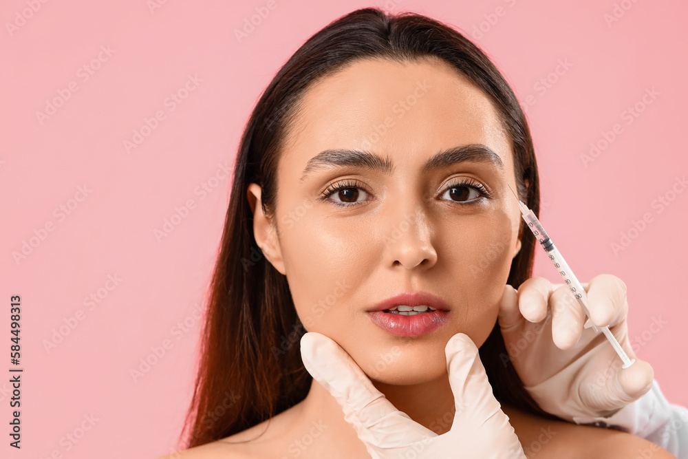 Young woman receiving filler injection in face against pink background