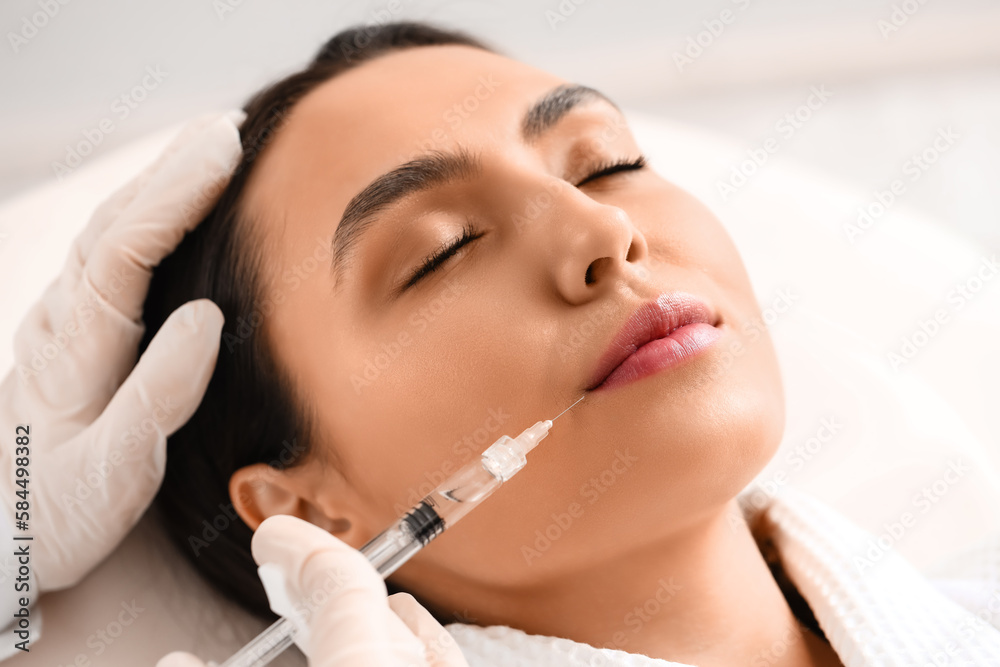 Young woman receiving filler injection in beauty  salon