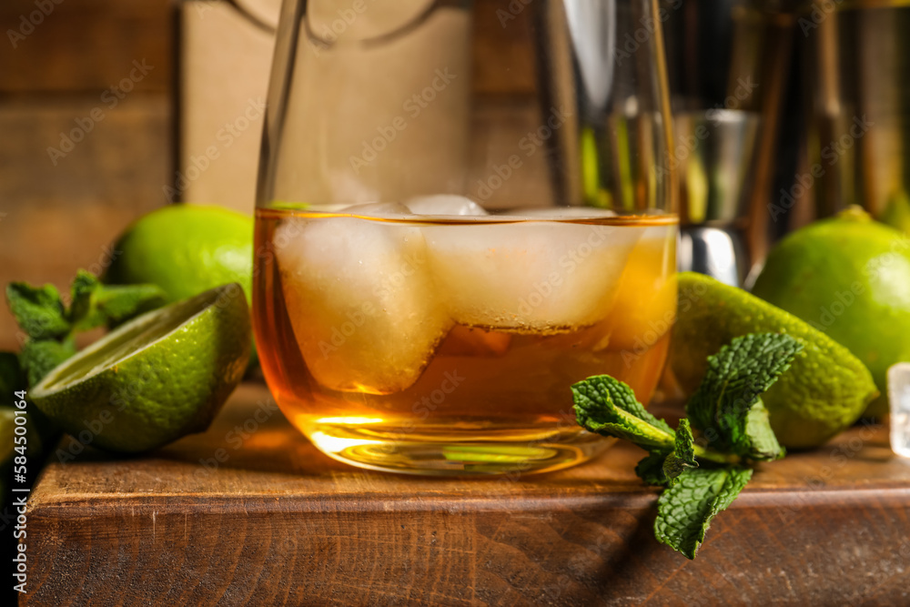 Glass of rum with ice, mint and lime on wooden table, closeup