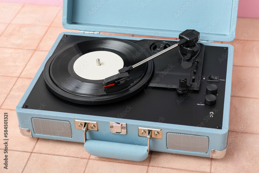 Record player with vinyl disk on table near pink wall, closeup