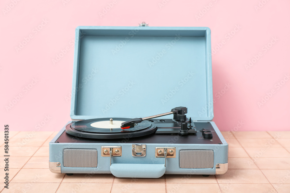 Record player with vinyl disk on table near pink wall