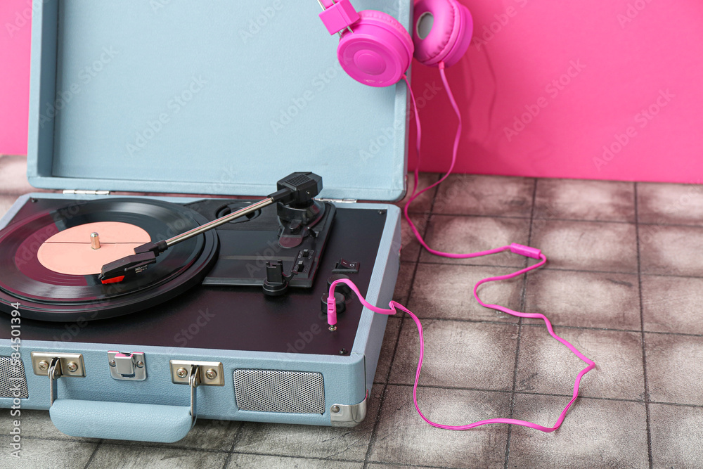 Record player with vinyl disk and headphones on table near pink wall, closeup