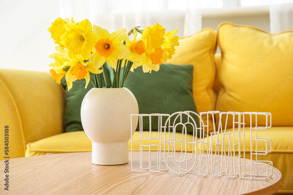 Vase with narcissus flowers and word HOME on coffee table in living room