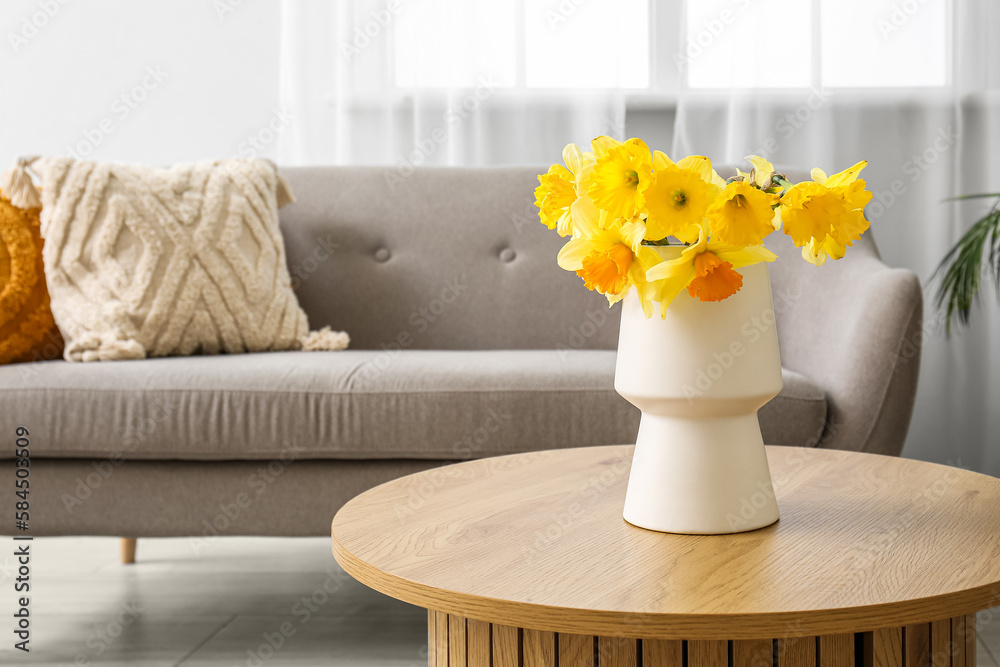 Vase with beautiful narcissus flowers on coffee table in cozy living room