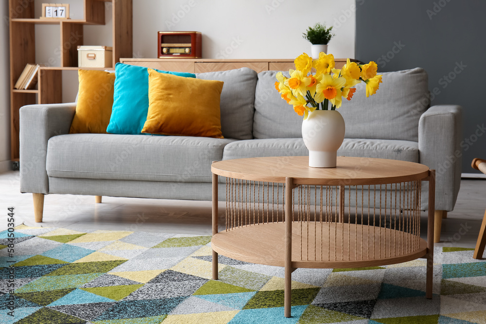 Vase with beautiful narcissus flowers on coffee table in stylish living room