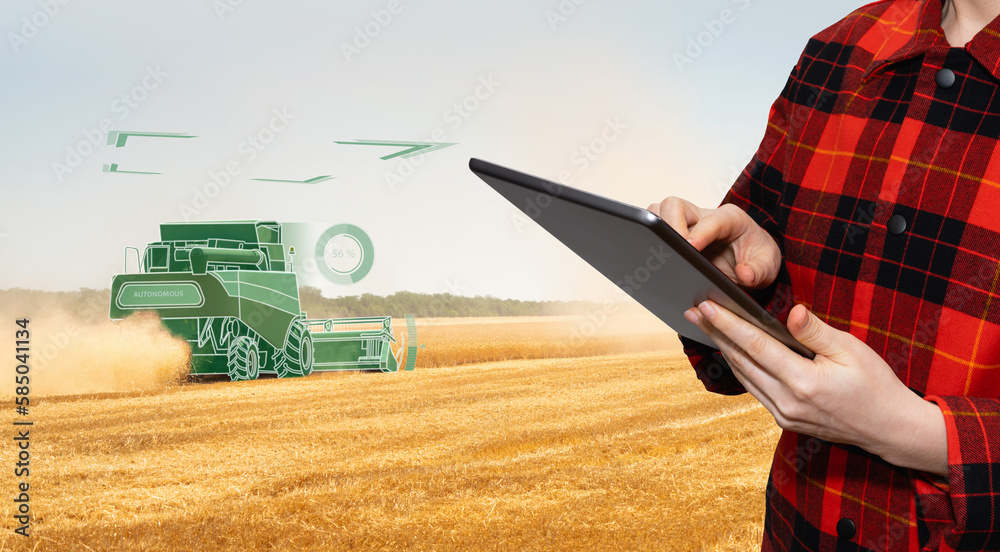 Farmer uses a digital tablet to control autonomous harvester. Smart farming concept.	