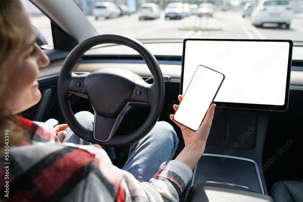  Woman driver in a car holds a smartphone with a white screen.