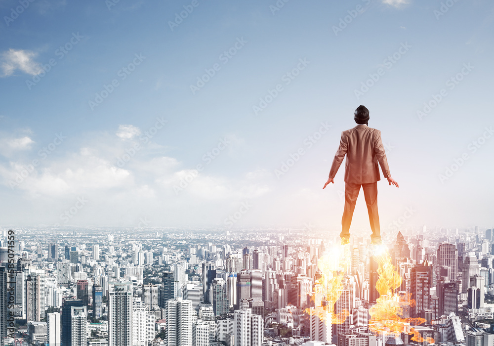 Businessman in suit and aviator hat flying in sky