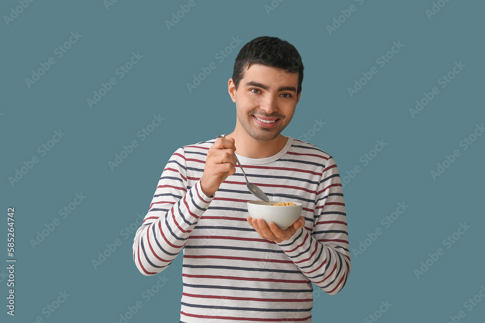 Young man eating cornflakes with spoon on color background