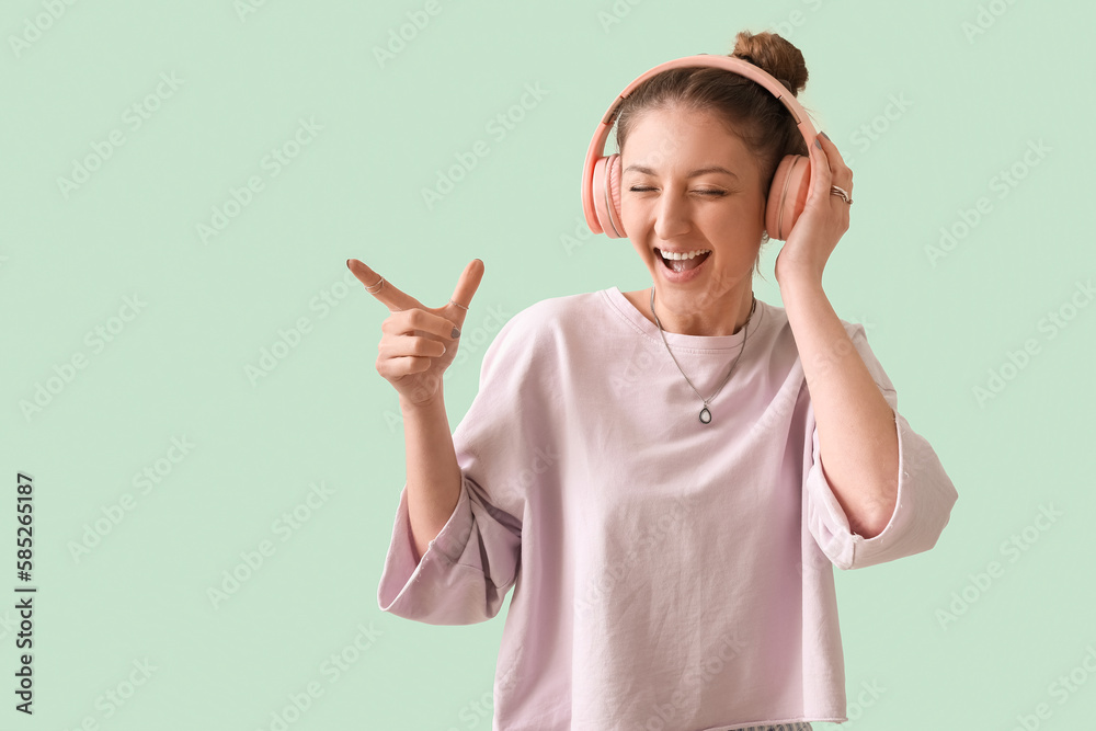 Young woman in headphones pointing at something on green background