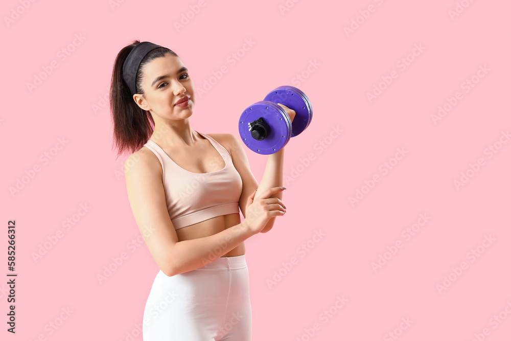 Sporty young woman with dumbbell on pink background