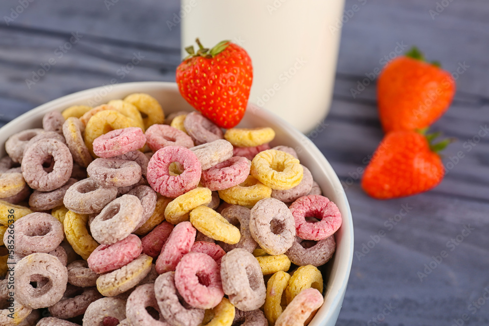 Bowl of colorful cereal rings with strawberries on blue wooden background