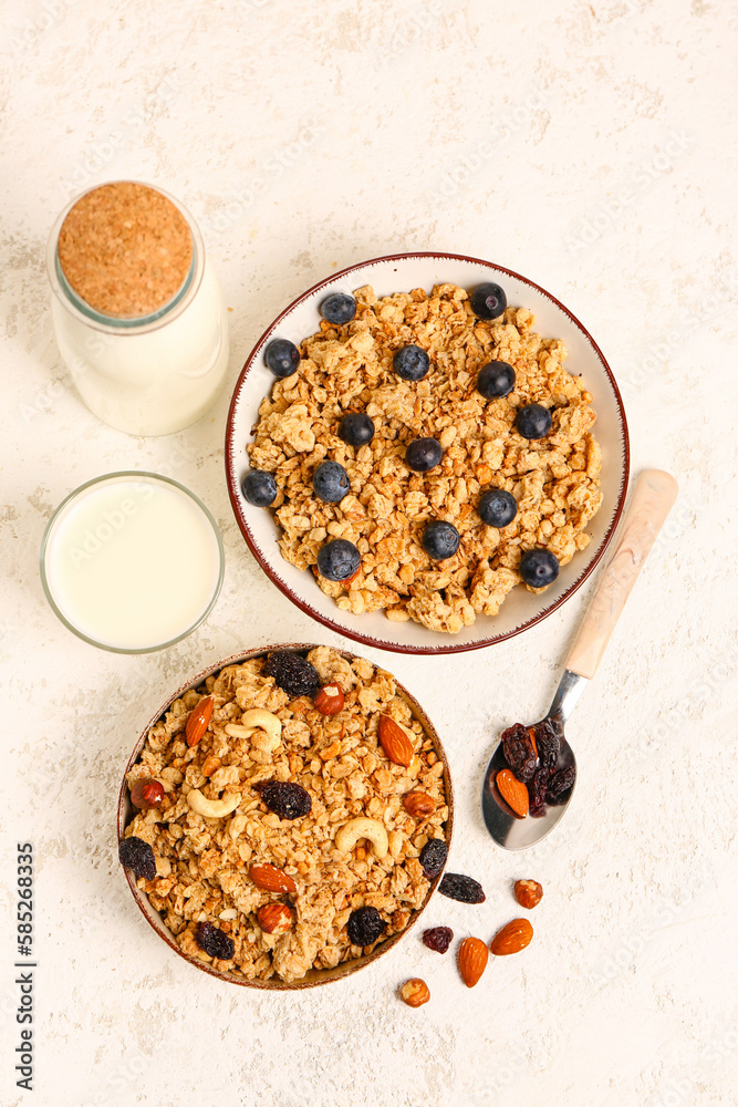 Bowls with tasty granola, bottle and glass of milk on light background