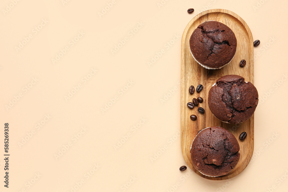 Wooden board with tasty chocolate cupcakes on beige background