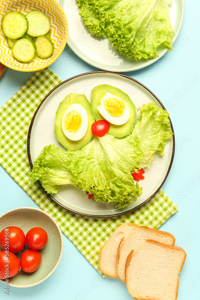 Plate with funny breakfast in shape of owl, vegetables and bread on blue background