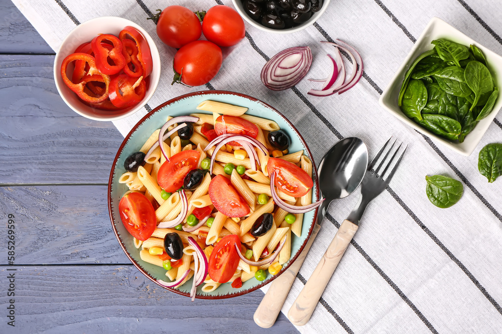 Bowl with tasty pasta salad and ingredients on blue wooden background