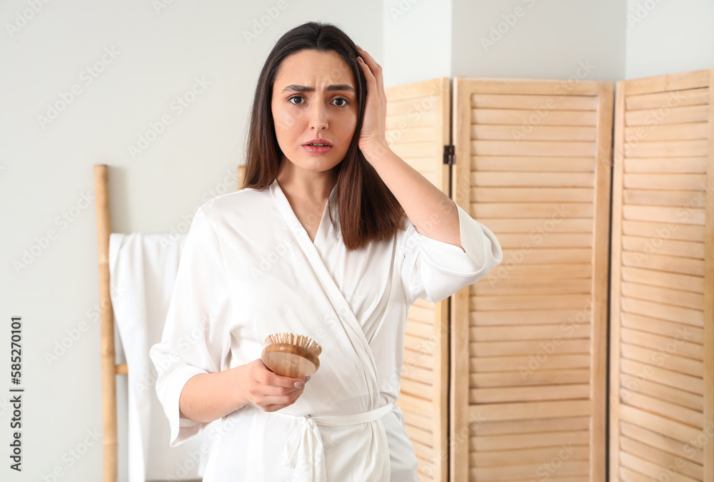 Worried young woman with hair loss problem in bathroom