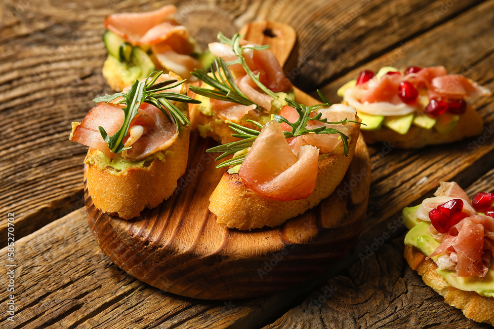 Board of tasty bruschettas with ham on wooden background