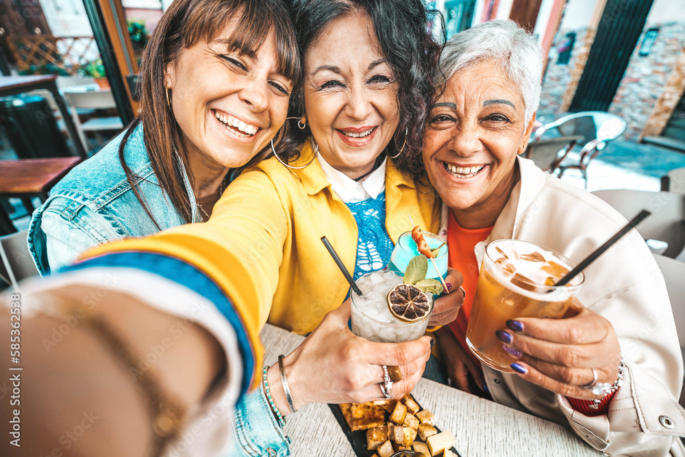 Happy senior women drinking cocktail glasses sitting at bar table - Group of best friends enjoying h