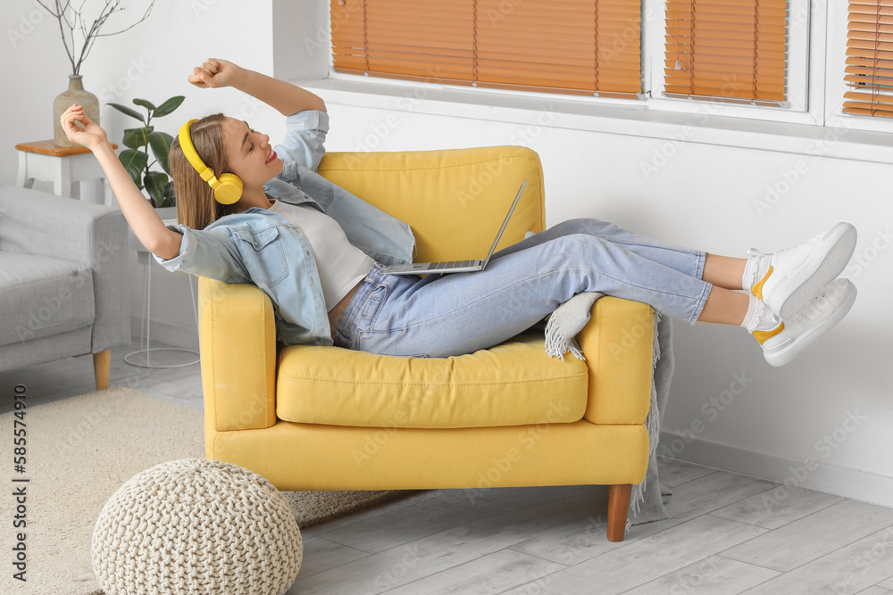 Young woman with headphones listening to music in yellow armchair at home