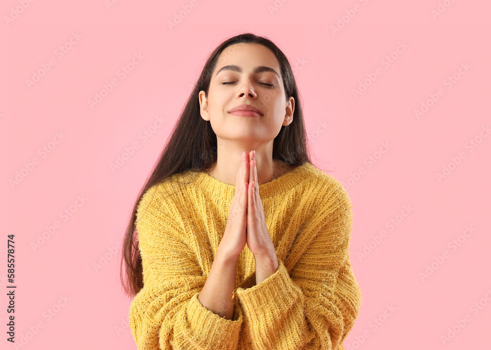 Beautiful young woman praying on pink background