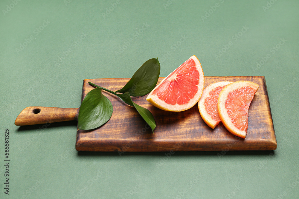 Wooden board with slices of ripe grapefruit and plant branch on green background