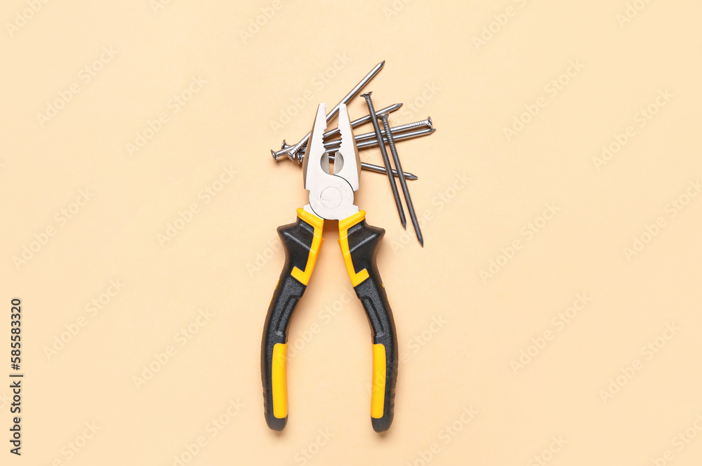 Pliers and nails on beige background