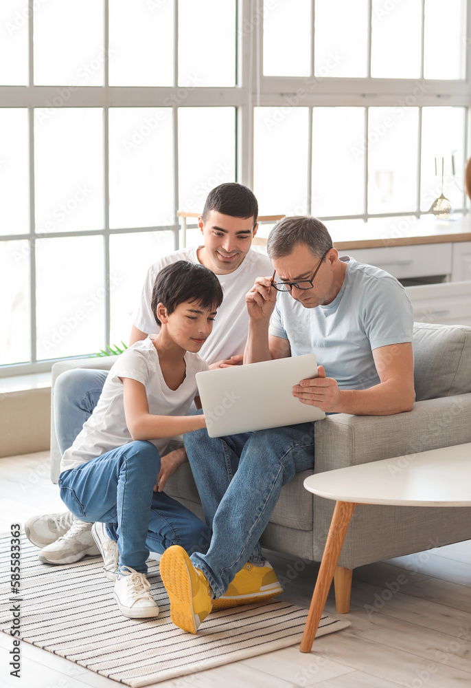 Happy little boy with his dad and grandfather using laptop at home