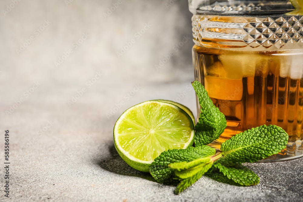 Glass of rum with ice, mint and lime on grey background, closeup