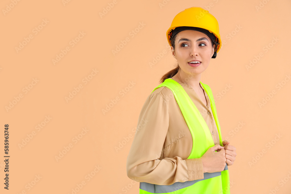 Female worker in vest and hardhat on beige background